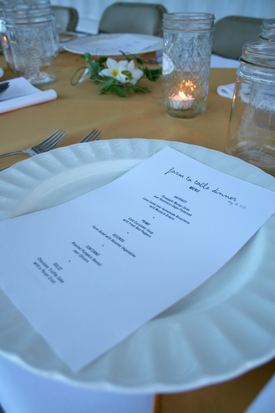 A menu rests on a plate of a formally set table with flowers, vines and candles.