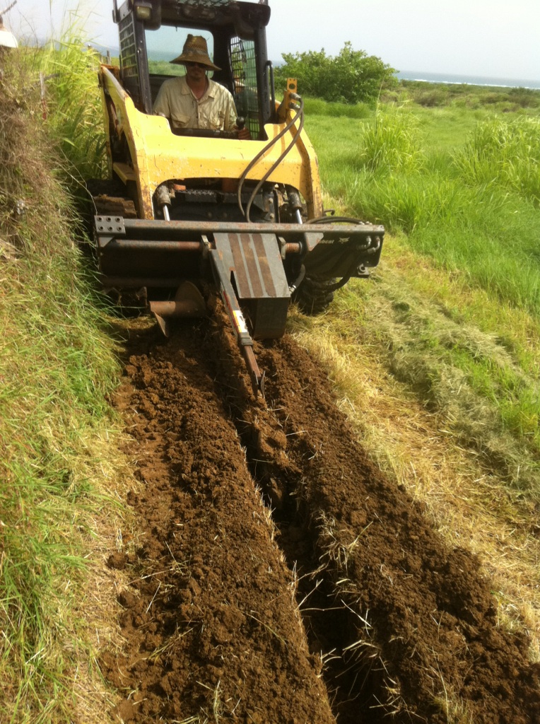 Luca operating a trencher on a skid steer in the pastures at ARTfarm