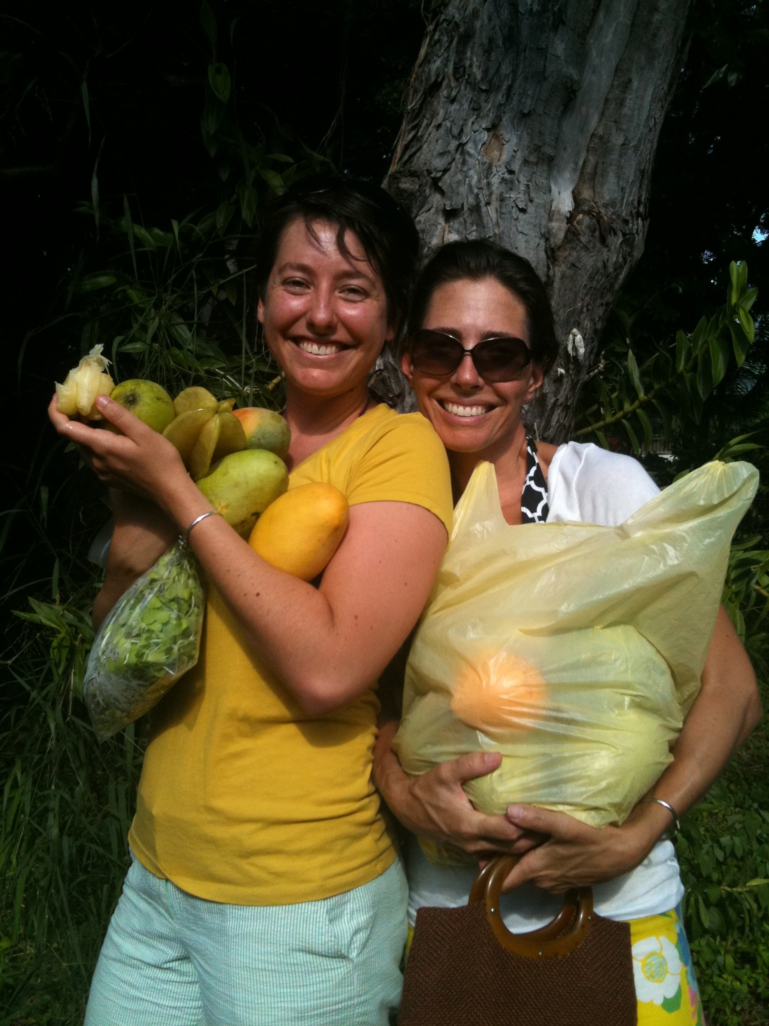 Two happy ladies laden down with microgreens and mangoes at the ARTfarm